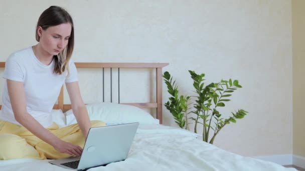 Mulher trabalhando em um laptop sentado na cama na casa . — Vídeo de Stock