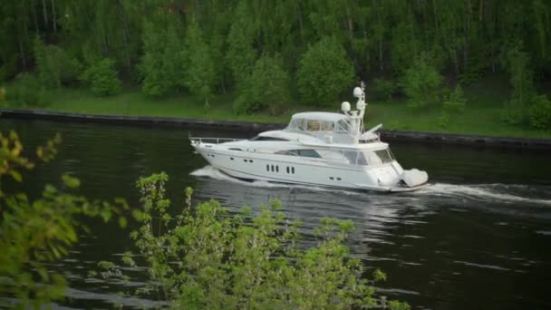 Подорожі, розкішний водний відпочинок на човні. Біла яхта повільно плаває вздовж бетонних берегів судноплавного каналу влітку серед зелених дерев на березі — стокове відео