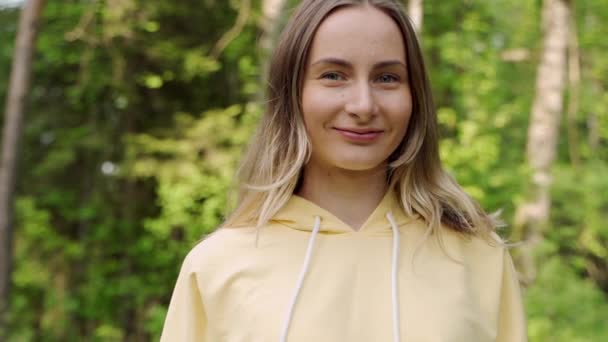 Молодая красивая женщина в спортивной одежде стоит в лесу, улыбается и позирует перед камерой — стоковое видео