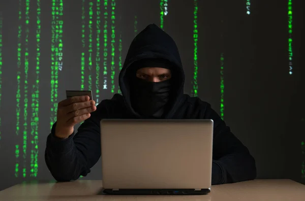 Computer hacker with credit card stealing data from a laptop concept for network security, identity theft and computer crime — Stock Photo, Image