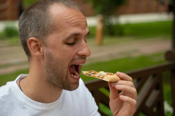 Красивый молодой человек ест пиццу на улице — стоковое фото