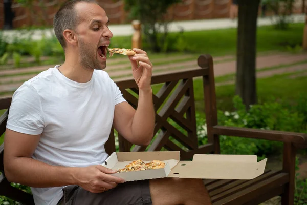 Красивый молодой человек ест пиццу на улице — стоковое фото