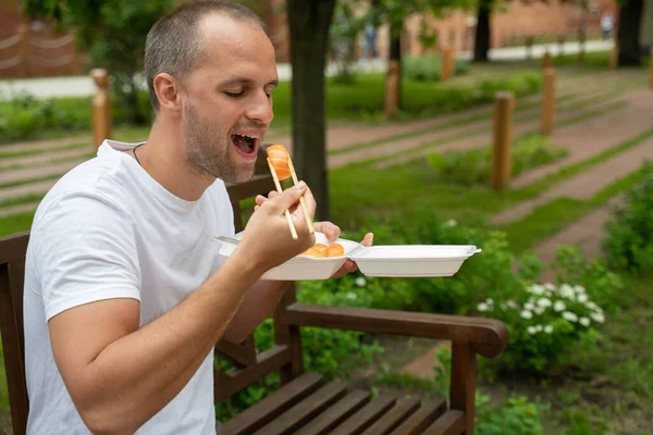 Молодой человек сидит снаружи и ест суши на вынос. — стоковое фото