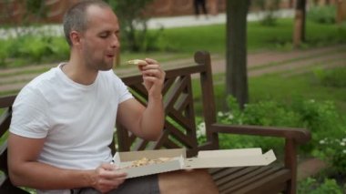 Yakışıklı genç adam sokakta pizza yiyor.