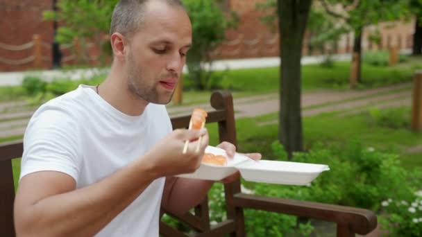 Facet siedzi na zewnątrz jedząc sushi na wynos. — Wideo stockowe