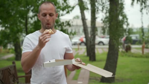 Schöner junger Mann isst ein Stück Pizza in der Straße — Stockvideo