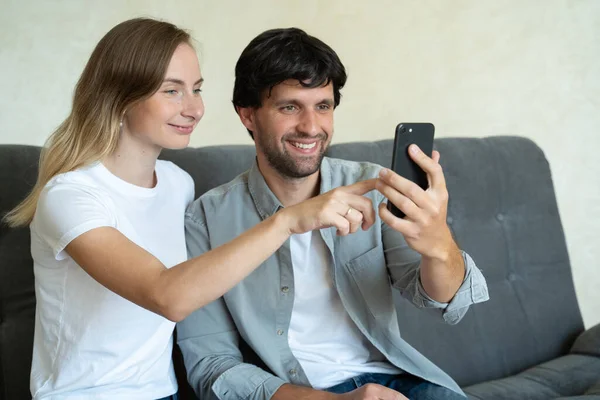Sonriendo joven pareja abrazando mientras mira el teléfono inteligente. Pareja compartiendo redes sociales en el teléfono inteligente . — Foto de Stock
