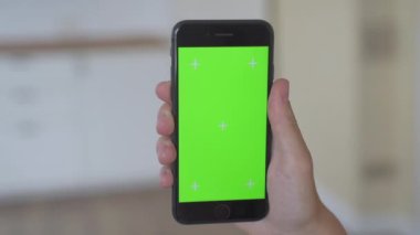 Dikey yeşil ekran cep telefonu kullanan bir kadın. Evde taşınabilir aletleri elinde tutan bir kadın var.. 