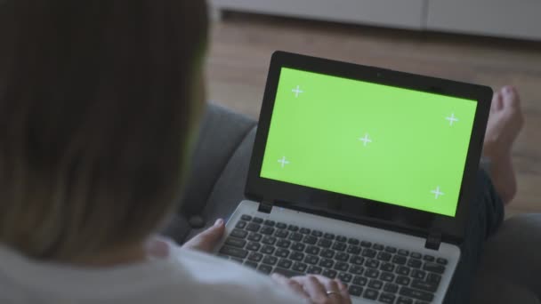Женщина сидит дома на диване, пробки на ноутбуке компьютер с зеленым макетом экрана. девушка с помощью компьютера, просмотр через Интернет, просмотр контента — стоковое видео