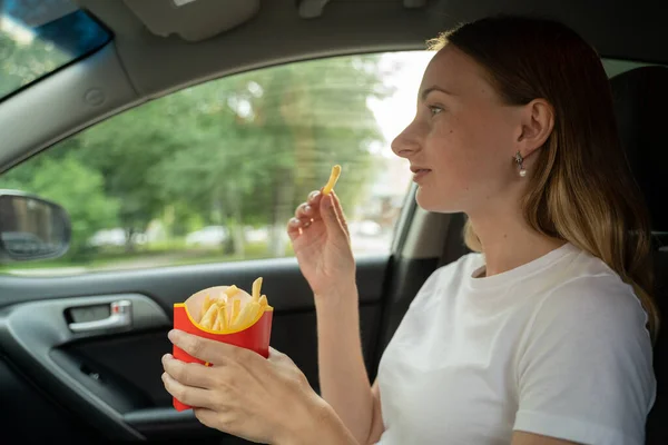 Female eating fries in the car. Hands holding a paper bag with fast food fried potatoes.