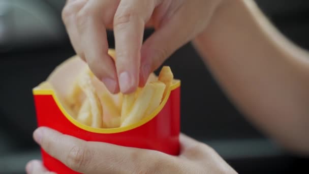 Honan äter pommes frites i bilen. Händerna håller en papperspåse med snabbmat stekt potatis. — Stockvideo