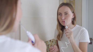 Diş telleriyle gülümseyen genç bir kadın. Dişlerini su temizleyicisiyle temizliyor.