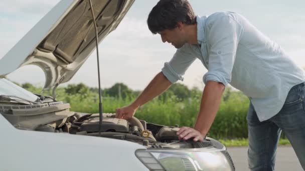 Homme debout à côté d'une voiture en panne, regardant le moteur dans la frustration — Video