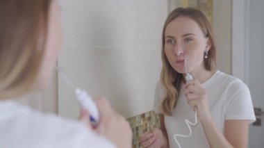 Diş telleriyle gülümseyen genç bir kadın. Dişlerini su temizleyicisiyle temizliyor.