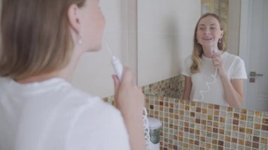 Diş telleriyle gülümseyen genç bir kadın. Dişlerini su temizleyicisiyle temizliyor.