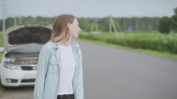 Jonge vrouw heeft een kapotte auto en ze vangt een passerende auto — Stockvideo