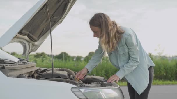 Жінка стоїть біля зламаної машини. Дівчина відкрила капот і подивилася на двигун . — стокове відео