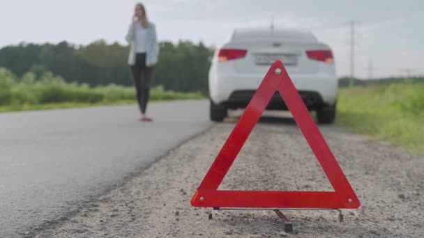 女性と三角形の警告サインを閉じてください背景に彼女の車と別れた後の支援を呼び出します — ストック動画
