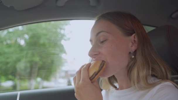 Голодная женщина ест бургеры сидя в машине, нездоровую пищу — стоковое видео