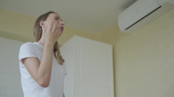 Mujer en su moderno apartamento en sala de estar. Enciende el aire acondicionado desde el mando a distancia. Climatización en casa con sistema split . — Vídeos de Stock