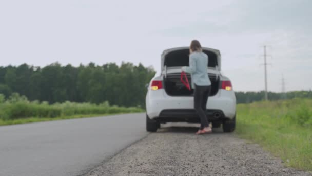 Mujer estresada poniendo una señal de emergencia en la carretera. Mujer con problemas con el coche, detuvo su vehículo en el borde de la carretera y espera ayuda — Vídeo de stock