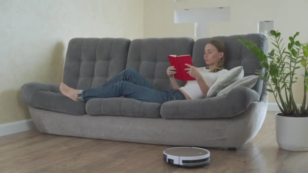 Femme lecture livre tandis que robot aspirateur nettoyage maison — Video