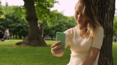 Görüntülü arama yapan akıllı telefonlu kadın yeşil parktaki sosyal mesafenin tadını çıkarıyor..