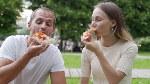 外でピザを食べる若いカップル。女と男は公園でピクニックをしている。ファーストフードのコンセプト. — ストック動画