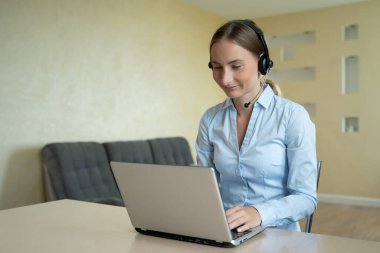 Konferans görüşmesiyle iletişim kuran kulaklık takan bir kadın ev ofisindeki bilgisayara bakıyor, görüntülü görüşme yapıyor.