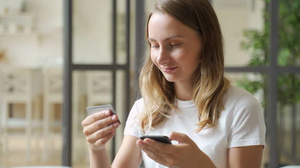 Mujer con tarjeta de crédito y smartphone. Mujer joven sentada en el sofá gastar dinero en casa, hacer el pedido, la compra a través de Internet, servicios comerciales, concepto de pago seguro en línea — Foto de Stock