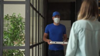 Koruyucu sağlık maskeli arkadaş canlısı pizza teslimatçısı evdeki müşteriye sipariş veriyor.