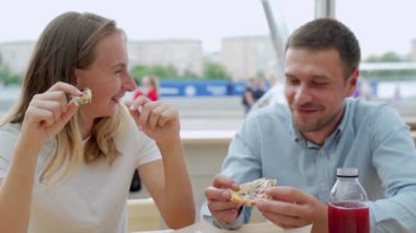 Dışarıda pizza yiyen ve gülümseyen bir çift. Açık bir kafede pizza yiyorlar..