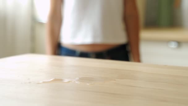 Ama de casa limpiando el café derramado o té de una mesa de cocina de madera. Hembra usando una toallita limpiadora doméstica para limpiar. — Vídeo de stock