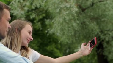 Gölün kenarında kendi portresini çeken genç bir çift. Erkek ve kadın akıllı telefonlarıyla selfie çekiyorlar..