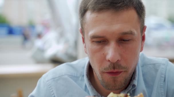 Красивий молодий чоловік їсть шматочок піци на вулиці — стокове відео
