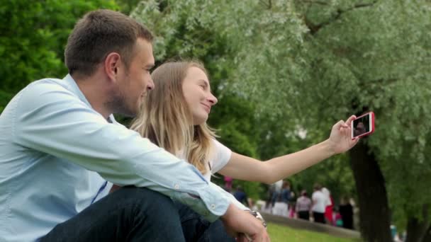 Gölün kenarında kendi portresini çeken genç bir çift. Erkek ve kadın akıllı telefonlarıyla selfie çekiyorlar.. — Stok video