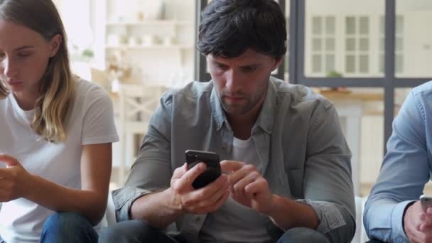 Group of three friends hanging out but ignoring each other while using their smartphones at home — Stock Video