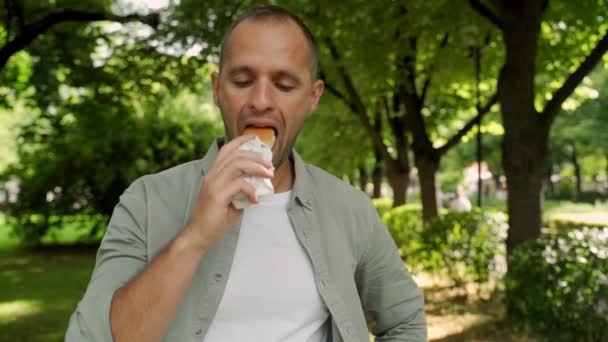 Hungrig man slukar en varmkorv på gatan — Stockvideo