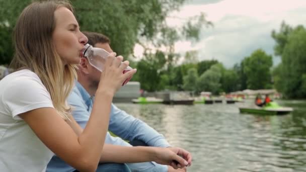 Giovane coppia è romantico nel parco su un lago. L'uomo e la donna siedono al sole estivo nell'erba verde — Video Stock
