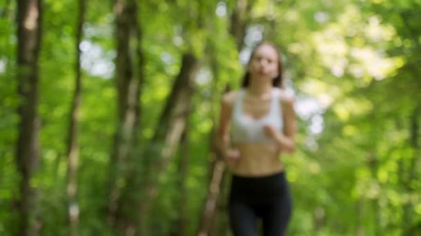 Een vermoeide jonge vrouw met oortjes loopt in het park. — Stockvideo