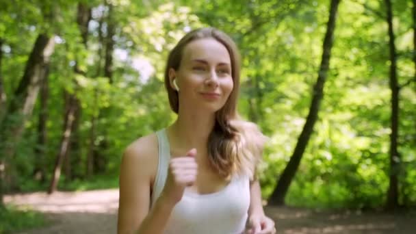 Atletische jonge vrouw met koptelefoon luisteren naar muziek en hardlopen in het park — Stockvideo