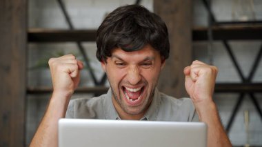 Mutlu galip. Genç heyecanlı adam koltukta otururken dizüstü bilgisayar kullanıyor..