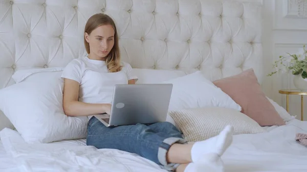 Mujer sonriente usando computadora portátil en la cama. Uso cotidiano del concepto de tecnología. — Foto de Stock