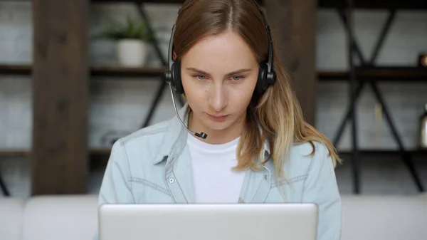年轻女人坐在家里，带着耳机在网上电脑上工作。在线学习或在家工作的概念 — 图库照片