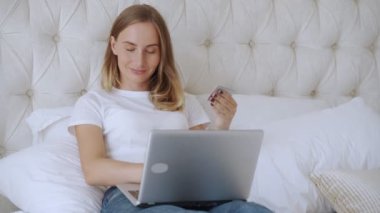 Kredi kartı tutan ve dizüstü bilgisayar kullanan bir kadın, evde yatakta oturan genç bir bayan, internet mağazasından alışveriş yapan bir müşteri.