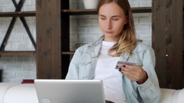 Mulher segurando cartão de crédito e usando laptop, sentado no sofá em casa, jovem cliente do sexo feminino compras on-line na loja de internet — Vídeo de Stock