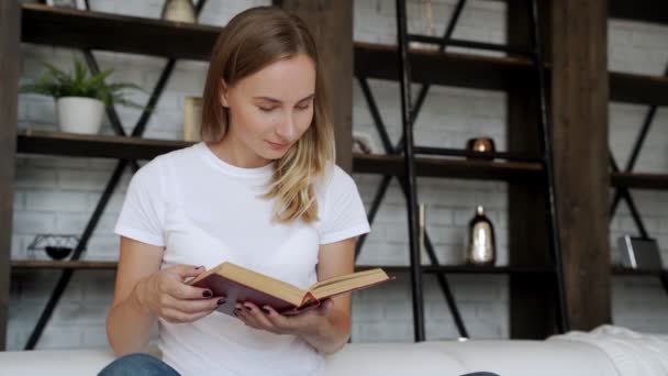 Mooie jonge vrouw die een boek leest op de bank. — Stockvideo