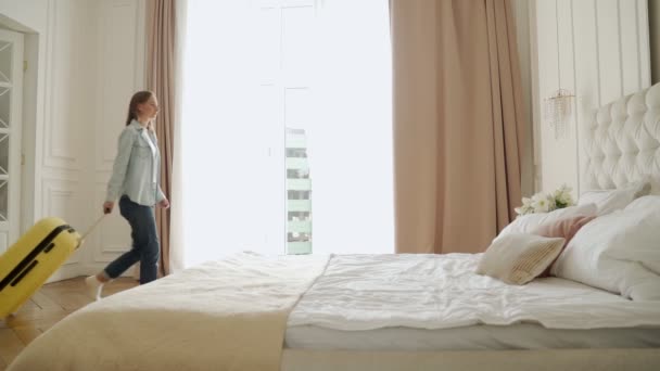 Kobieta wchodząca do pokoju hotelowego z walizką i upadająca na łóżko zmęczona. — Wideo stockowe