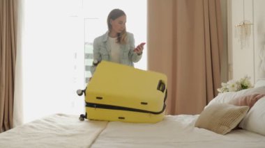 Kadın otel odasında sarı bavul hazırlıyor.