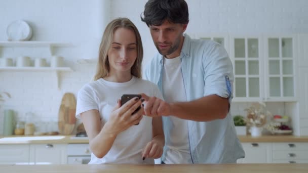 Paar aan tafel in de keuken check loterij on-line app op smartphone zie monetaire overwinning voelt opgewonden vieren moment van overwinning. — Stockvideo